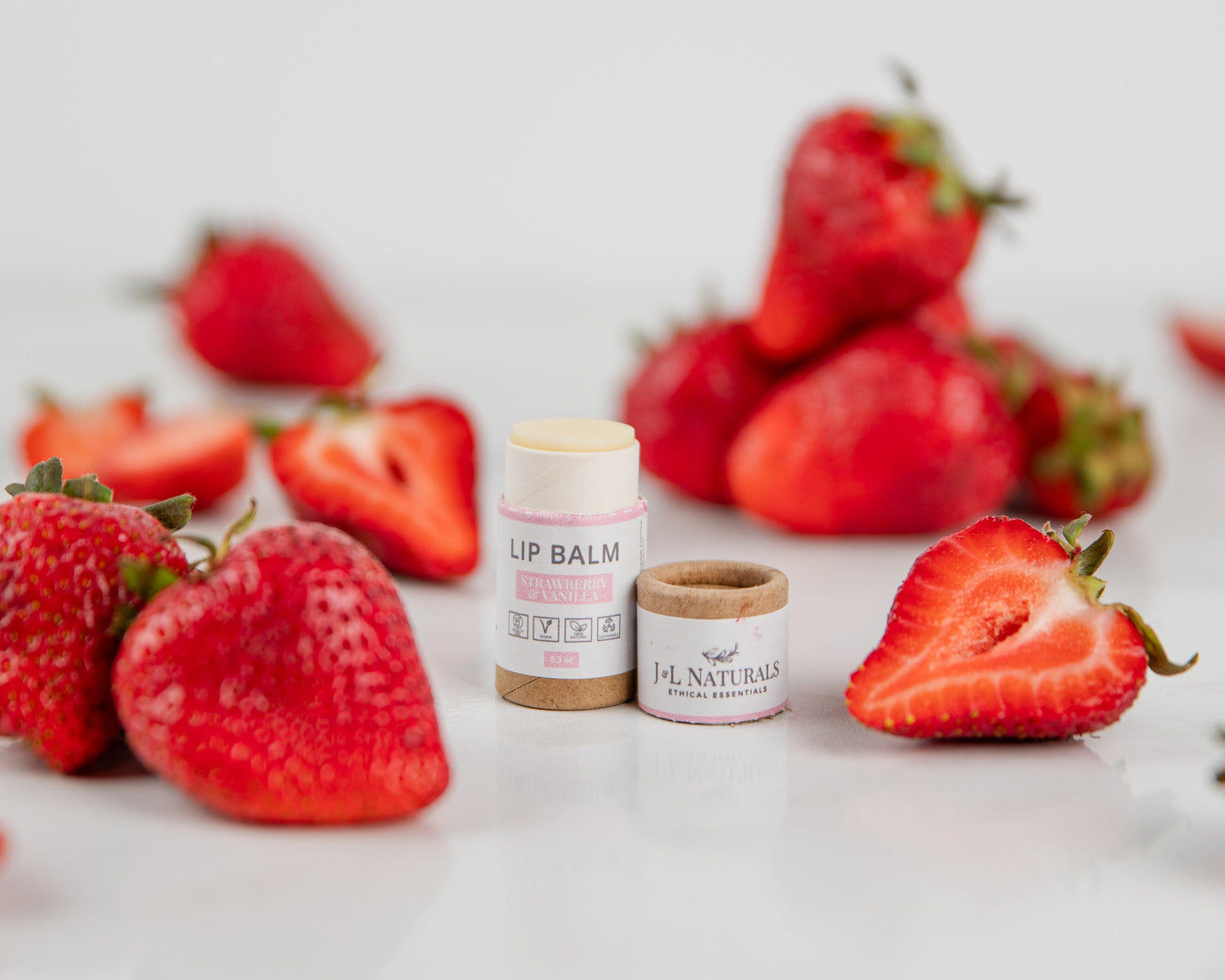 Lip Balm Strawberry and Vanilla alongside fresh strawberries