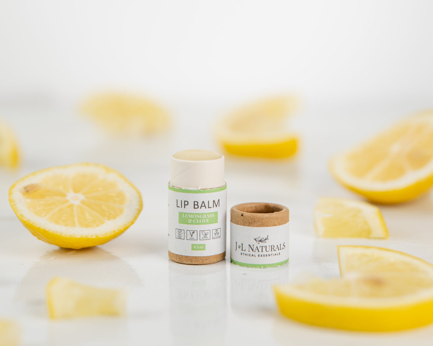 Lemongrass & Clove Lip Balm alongside array of lemons